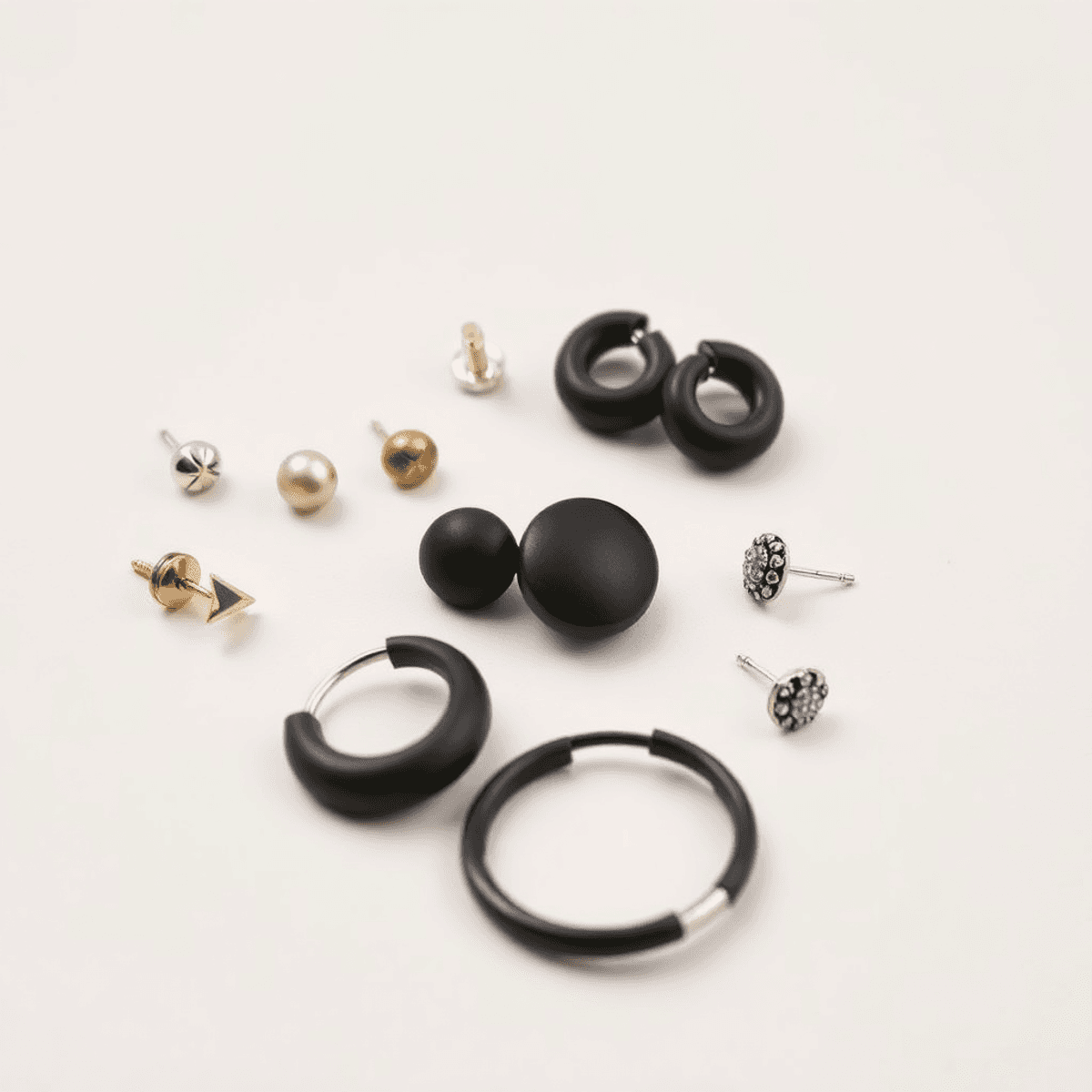Close-up of various men's earrings on a neutral background, featuring minimalist studs and bold hoops, highlighting modern fashion and self-expression.